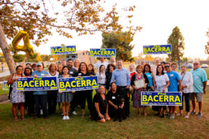 Campaign supporters gather in a park holding "Re-Elect Phil Bacerra" signs and a certificate during a group photo celebrating his Santa Ana City Council Ward 4 campaign.